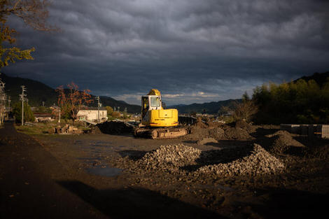 Earth mover sitting atop hill bright in the last of the day's light, dark stormy skies behind.