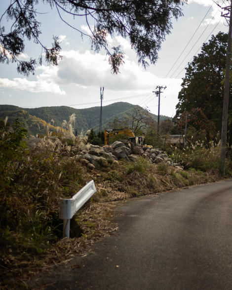 Road, brush off to the left, guardrail, digger back behind a mound of rocks.