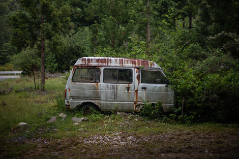 A van, once white, now rust-stained, abandoned in a bush.