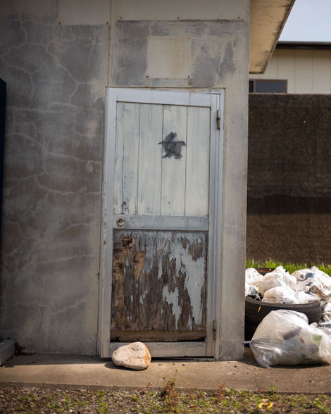 A toiler door with the kanji for woman on it, held closed by a rock on the ground. 