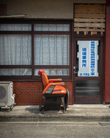 A pleather barber's chair sitting out in the street in front of, presumably, the barber shop in which it once sat.