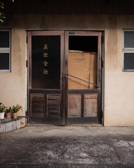 Slightly ajar door to abandoned office, cardboard in doorway, potted plants on the ground.