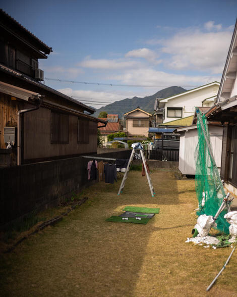 A peek into a residential yard, two ladders converted into a clothes line, shirts and pants drying in the sun, some golf balls siting on a fake green in the foreground.