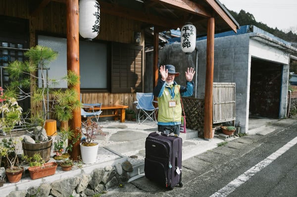 A man waving goodbye in front of Minshuku Tsugizakura